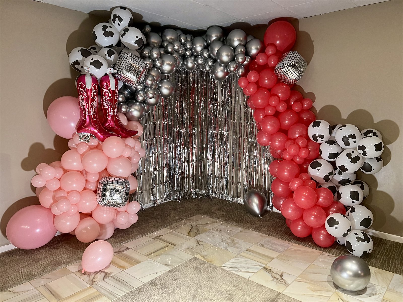 Pink, red, silver, and cow-print balloon installation with disco ball accents