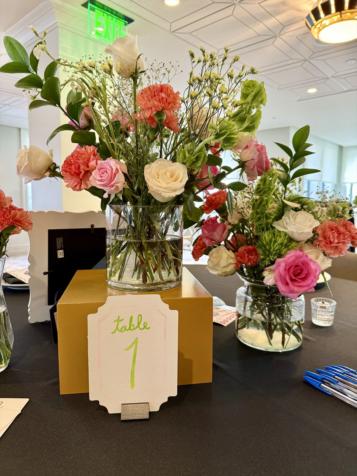 Pink, white, and green floral arrangements with a hand-lettered Table 1 sign